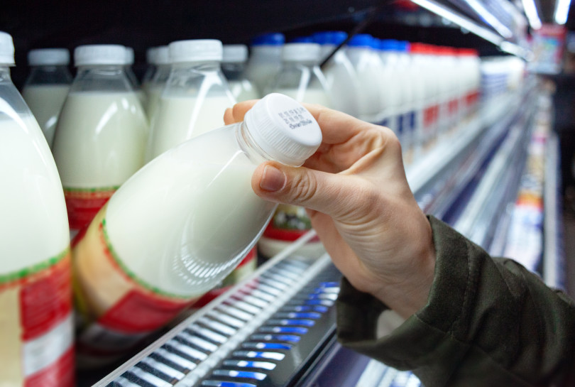 Womans hand holding milk bottle in supermarket. Man shopping mil