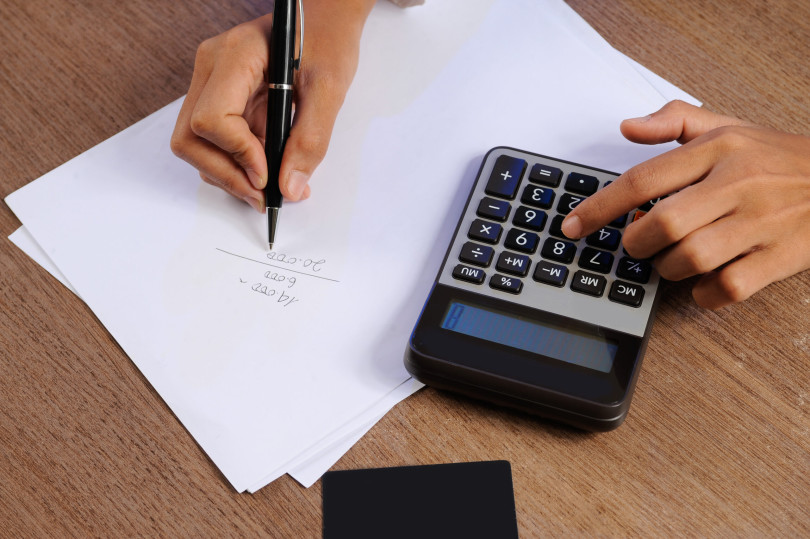 Closeup of person calculating on calculator and writing. Credit card, paper sheet and calculator lying on desk. Accountancy concept. Cropped view.